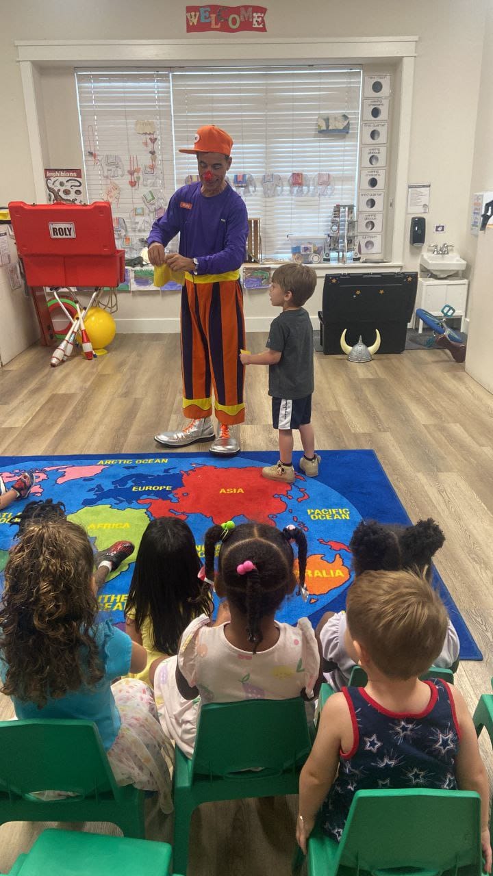Rolly the Clown making a balloon for a boy as children watch from their chairs.