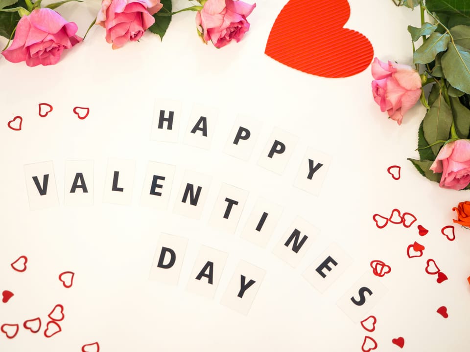Letter tiles spelling "Happy Valentine's Day" surrounded by pink roses and red hearts.