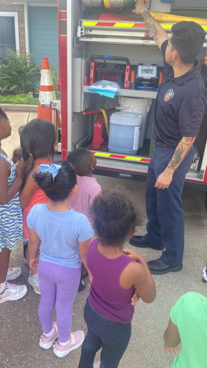 A firefighter showing children the equipment stored on the side of a fire truck.