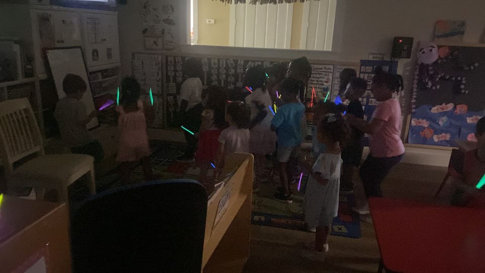 Children dancing with glow sticks in a darkened classroom.